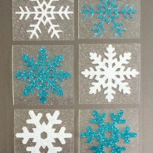 May include: Six clear plastic squares with snowflake stickers. Three snowflakes are white with glitter and three are blue with glitter.