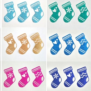 Peut inclure: Une collection d'ornements de bas de Noël scintillants de différentes couleurs, dont le rouge, le bleu, le vert, le rose, l'or, le violet et le magenta. Chaque bas de Noël présente un motif unique, comme des flocons de neige, des cœurs et des zigzags.