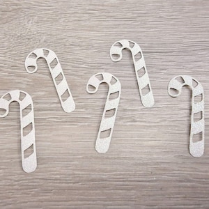 May include: Five white paper candy cane cutouts with a striped pattern. The cutouts are on a woodgrain background.