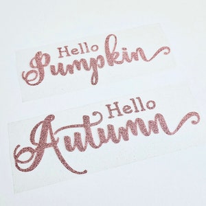 Könnte beinhalten: Zwei rosa Glitzer-Vinyl-Aufkleber mit dem Text "Hello Pumpkin" und "Hello Autumn" in einer kursivschrift.