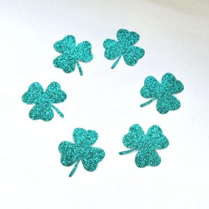 Op de afbeelding: Zes teal glitter klavertje vier vormen op een witte achtergrond.