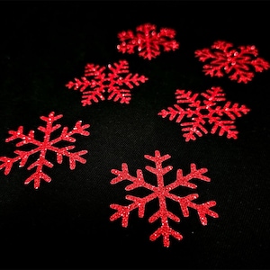 Peut inclure: Six flocons de neige rouges pailletés sur un fond noir. Les flocons de neige sont de tailles et de formes différentes.