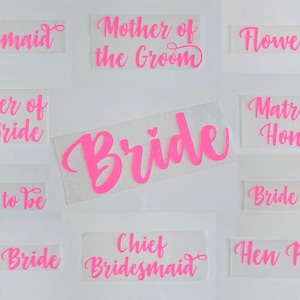 May include: Pink vinyl stickers with various wedding party titles, including "Bride", "Bridesmaid", "Mother of the Bride", "Mother of the Groom", "Chief Bridesmaid", "Bride Squad", "Team Bride", "Matron of Honour", "Flower Girl", and "Hen Party".