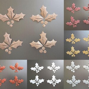 Könnte beinhalten: Eine Sammlung glitzernder Stechpalmenblatt- und Beeren-Dekorationen in verschiedenen Farben. Das Bild zeigt Blattsätze in Gold, Rosa, Rot, Weiß und Silber, ideal für Bastelarbeiten und Verzierungen für die Feiertage.