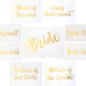 Könnte beinhalten: Goldfolien-Bügeletiketten mit verschiedenen Hochzeits-Party-Titeln, darunter "Bride", "Maid of Honour", "Chief Bridesmaid", "Bridesmaid", "Flower Girl", "Team Bride", "Bride Squad", "Mother of the Bride" und "Mother of the Groom".
