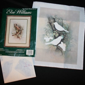 May include: Colorart Cross Stitch kit featuring a design by Elsa Williams. The kit includes a white Aida cloth with a printed design of two white birds perched on a tree branch with green leaves and white flowers. The kit also includes a color chart and instructions.