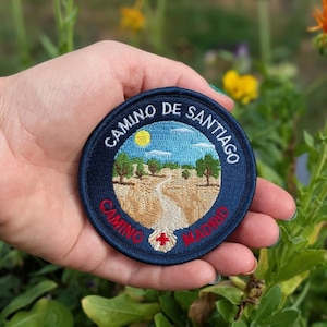 Puede incluir: Una taza de cerámica blanca con un asa negra y el texto "But First, Coffee" en negrita negra. La taza está sobre un fondo borroso, sugiriendo un ambiente acogedor.