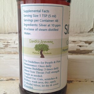 May include: A brown glass bottle with a white label that reads "Earth's Answers Natural Products". The label also includes the text "Supplemental Facts", "Serving Size 1 TSP (5 ml)", "Servings per Container: 48", "Ingredients: Silver at 10 ppm", "In a base of steam distilled Water.", and "Use Guidelines for People & Pets".