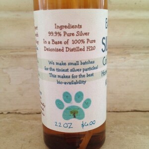 May include: A clear glass bottle with a white label that reads "Ingredients: 99.9% Pure Silver In a Base of 100% Pure Deionized Distilled H2O We make small batches for the tiniest silver particles! This makes for the best bio-availability 2.2 OZ $6.00". The bottle has a blue paw print with a tree inside on the label.