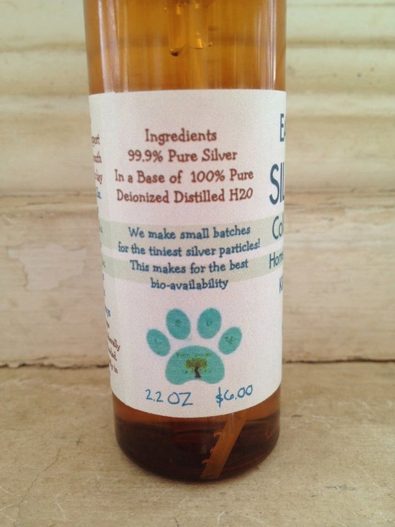 May include: A clear glass bottle with a white label that reads "Ingredients: 99.9% Pure Silver In a Base of 100% Pure Deionized Distilled H2O We make small batches for the tiniest silver particles! This makes for the best bio-availability 2.2 OZ $6.00". The bottle has a blue paw print with a tree inside on the label.