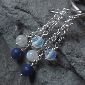 Peut inclure: Boucles d'oreilles en chaîne argent avec des perles de pierres précieuses bleues et blanches. Les boucles d'oreilles ont trois perles sur chaque chaîne, avec deux perles bleues et une perle blanche.