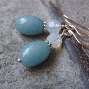 Peut inclure: Une paire de boucles d'oreilles avec des pierres ovales bleu clair et des perles facettées transparentes. Les boucles d'oreilles ont des crochets argentés.