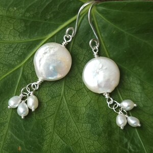 May include: A pair of silver dangle earrings with large white pearl drops and smaller white pearl accents.