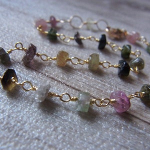 May include: A gold chain bracelet with a variety of colorful gemstones, including pink, green, and blue.