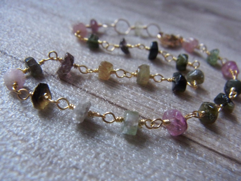 May include: A gold chain bracelet with a variety of colorful gemstones, including pink, green, and blue.