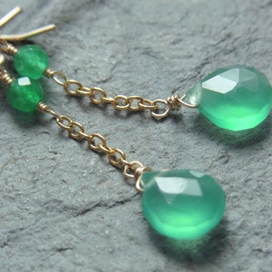 May include: A pair of green gemstone earrings with a gold chain and small green beads. The earrings are teardrop shaped.