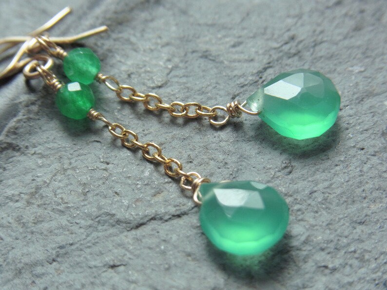 May include: A pair of green gemstone earrings with a gold chain and small green beads. The earrings are teardrop shaped.