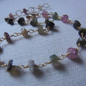 May include: A gold chain bracelet with a variety of small, colorful gemstones. The gemstones are pink, green, and black.