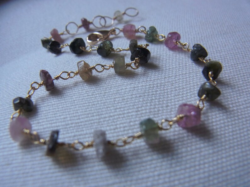 May include: A gold chain bracelet with a variety of small, colorful gemstones. The gemstones are pink, green, and black.