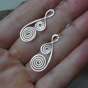 May include: A pair of silver earrings with a double spiral design. The earrings are dangle style and have a simple, elegant look.