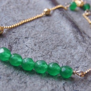 May include: A gold chain bracelet with a slider clasp and green gemstone beads.