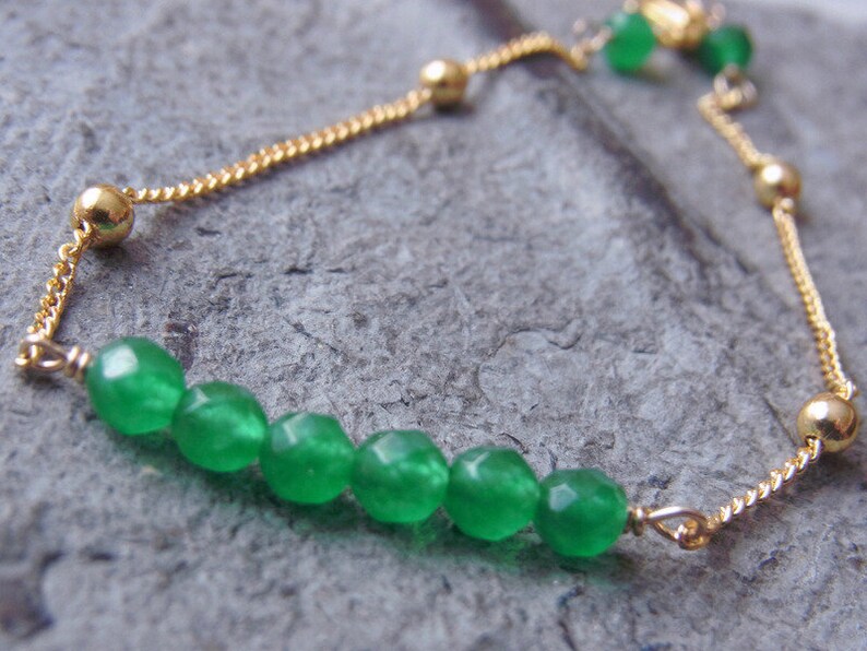 May include: A gold chain bracelet with a slider clasp and green gemstone beads.