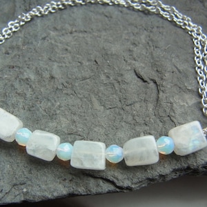 Peut inclure: Un collier en chaîne argent avec une rangée de perles de pierre de lune blanche et de perles irisées claires.