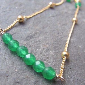May include: A gold chain bracelet with a green gemstone slider. The bracelet features a delicate chain and small gold beads.