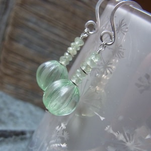 May include: A pair of silver earrings with green gemstone beads. The earrings feature a teardrop-shaped bead at the bottom and a series of smaller beads leading up to the silver hook.