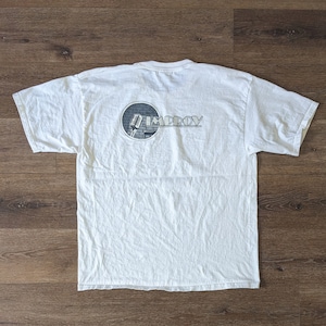 Op de afbeelding: Wit T-shirt met een zwart-witte afbeelding van een microfoon voor een bakstenen muur. De afbeelding bevindt zich in een cirkel met het woord "IMPROV" erboven.