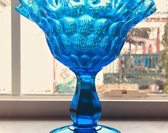 May include: A blue glass candy dish with a ruffled rim and a textured, bubbled design. The dish has a pedestal base.
