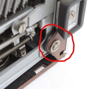 May include: Close-up of a typewriter with a brown leather roller and a silver screw. The roller is part of the typewriter's mechanism and is circled in red.