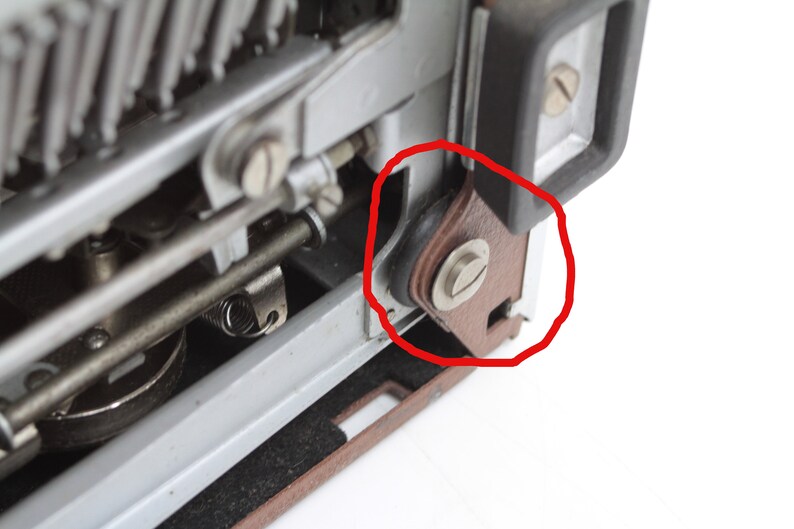 May include: Close-up of a typewriter with a brown leather roller and a silver screw. The roller is part of the typewriter's mechanism and is circled in red.