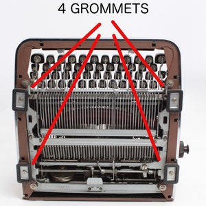 May include: A close-up view of the back of a vintage typewriter with the text "4 GROMMETS" written above the machine. The grommets are visible on the top of the typewriter.
