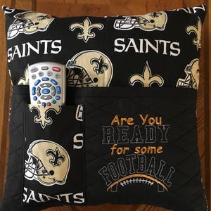 May include: Black and gold pillow with a Saints logo and the text "Are You Ready for Some Football". The pillow has a pocket on the side for a remote control.