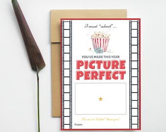 May include: A red and white card with a film strip border. The card features a cartoon illustration of a bucket of popcorn and movie tickets. The text on the card reads "I must "admil"... You've made this year Picture Perfect. No one is "butter" than you!"