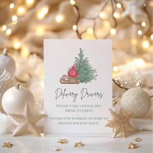 May include: A white card with a green Christmas tree and a red gift on a sled. The text on the card reads "Delivery Drivers Please take a snack and drink to enjoy! Thanks for working so hard to deliver holiday magic."