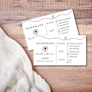 May include: A white care label with black text and checkboxes. The label says "Handmade" and includes instructions for washing, drying, and ironing. The label says "handle with care" and lists the materials as "100% Extra Fine Wool".
