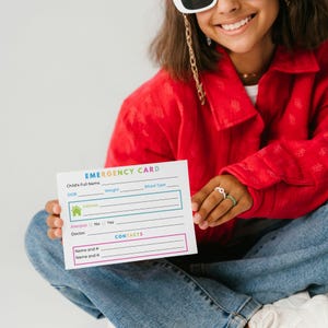 May include: A rectangular white emergency card with colorful text and lines for information. The card features fields for child's full name, DOB, weight, blood type, address, allergies, doctor, and contact names and phone numbers.