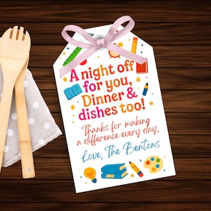 Könnte beinhalten: Ein weißes Geschenk-Etikett mit rosa Schleife, mit dem Text "A night off for you, Dinner & dishes too!" und einer Dankesbotschaft. Das Etikett ist mit Illustrationen zum Thema Schule verziert. Holzlöffel und ein gepunktetes Tuch im Hintergrund.