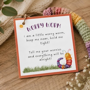 May include: A square white tag with a thin orange border, featuring the text WORRY WORM and a poem about holding the worm tight. A small yellow sun icon is in the top left, and a colorful, multi-segmented worm illustration sits on green grass.