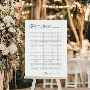 May include: A white sign on an easel with the text "First Dance Sweepstakes." The sign lists song titles and spaces for guests to write their names. The sign is decorated with elegant script and floral arrangements.