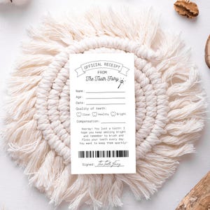 May include: A white "Official Receipt From The Tooth Fairy" card with fill-in-the-blank fields for name, age, and date, and a section for tooth quality. The card is on a cream-colored macrame coaster.