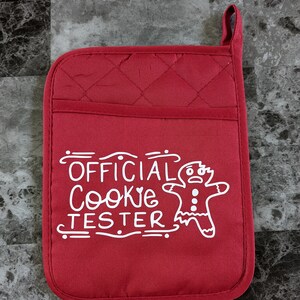 May include: Red quilted oven mitt with a white design that says "OFFICIAL COOKIE TESTER" with a gingerbread man graphic.