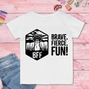 Puede incluir: Camiseta blanca con un gr&aacute;fico en blanco y negro de un hur&oacute;n dentro de un hex&aacute;gono con las letras "BFF". Las palabras "BRAVE. FIERCE. FUN!" est&aacute;n impresas en negro. Tambi&eacute;n se ven unos vaqueros azules y rotuladores de colores.