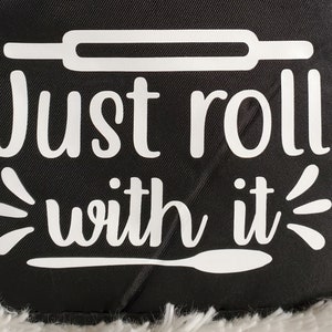 May include: Black kitchen towel with white text that reads "Just roll with it". The text is accompanied by a rolling pin and a spoon graphic.