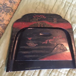 May include: Black and red decorative tray with a landscape design. The tray features a handle and the words "Yellowstone Park" at the bottom. The landscape includes trees, a bridge, and a boat.