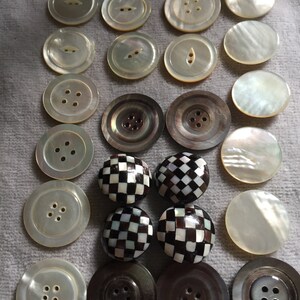 May include: A collection of 20 vintage buttons in various colours and patterns, including white, black, and brown. The buttons are made of different materials, such as mother of pearl and plastic. Some buttons have a chequered pattern, while others have a simple design.