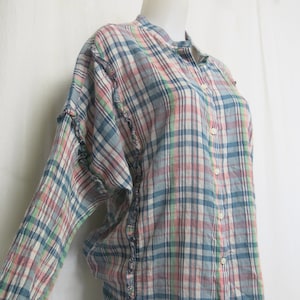 May include: A long-sleeved, button-up shirt with a plaid pattern in shades of blue, pink, green, and white. The shirt has a ruffled trim along the edges.