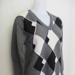 May include: A gray sweater with a black and white diamond pattern. The sweater has a v-neck and long sleeves.